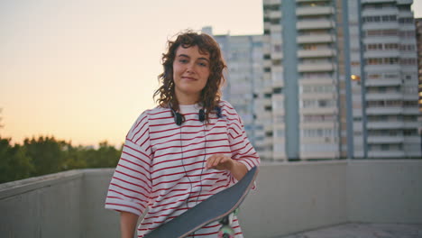 cool skater posing skateboard on city building roof at evening weekend close up