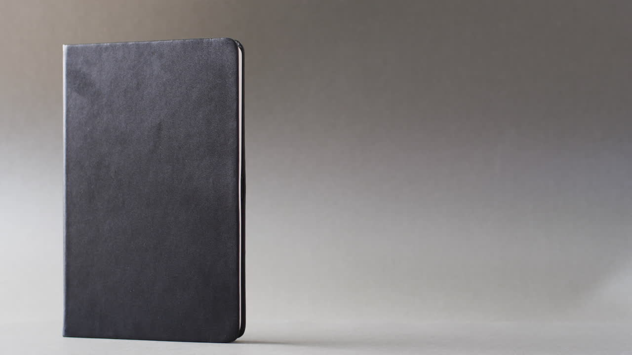 Close up of closed black book standing vertical with copy space on gray background in slow motion