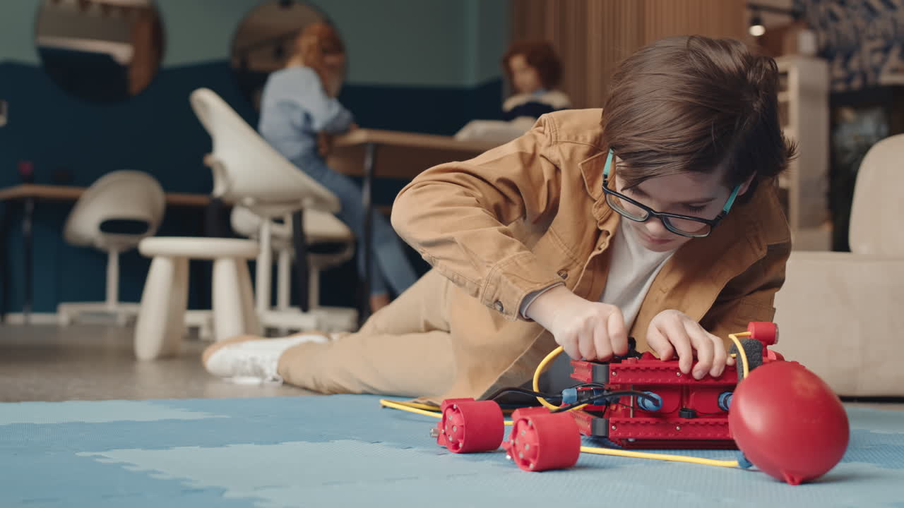 Young boy assembling a robotics kit on the floor in a classroom