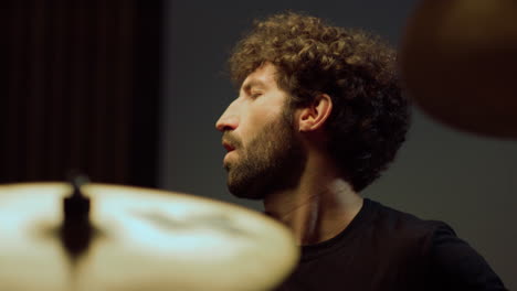 Portrait-of-bearded-drummer-performing-solo-on-drum-cymbals-in-recording-studio.