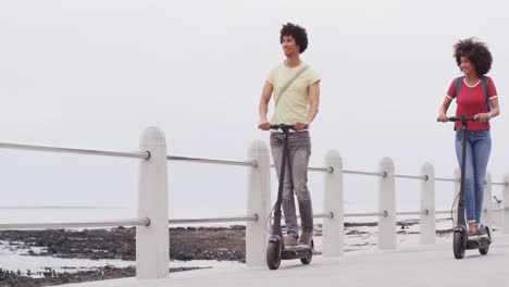 joven pareja afroamericana conduciendo scooters juntos en el paseo marítimo cerca de la playa