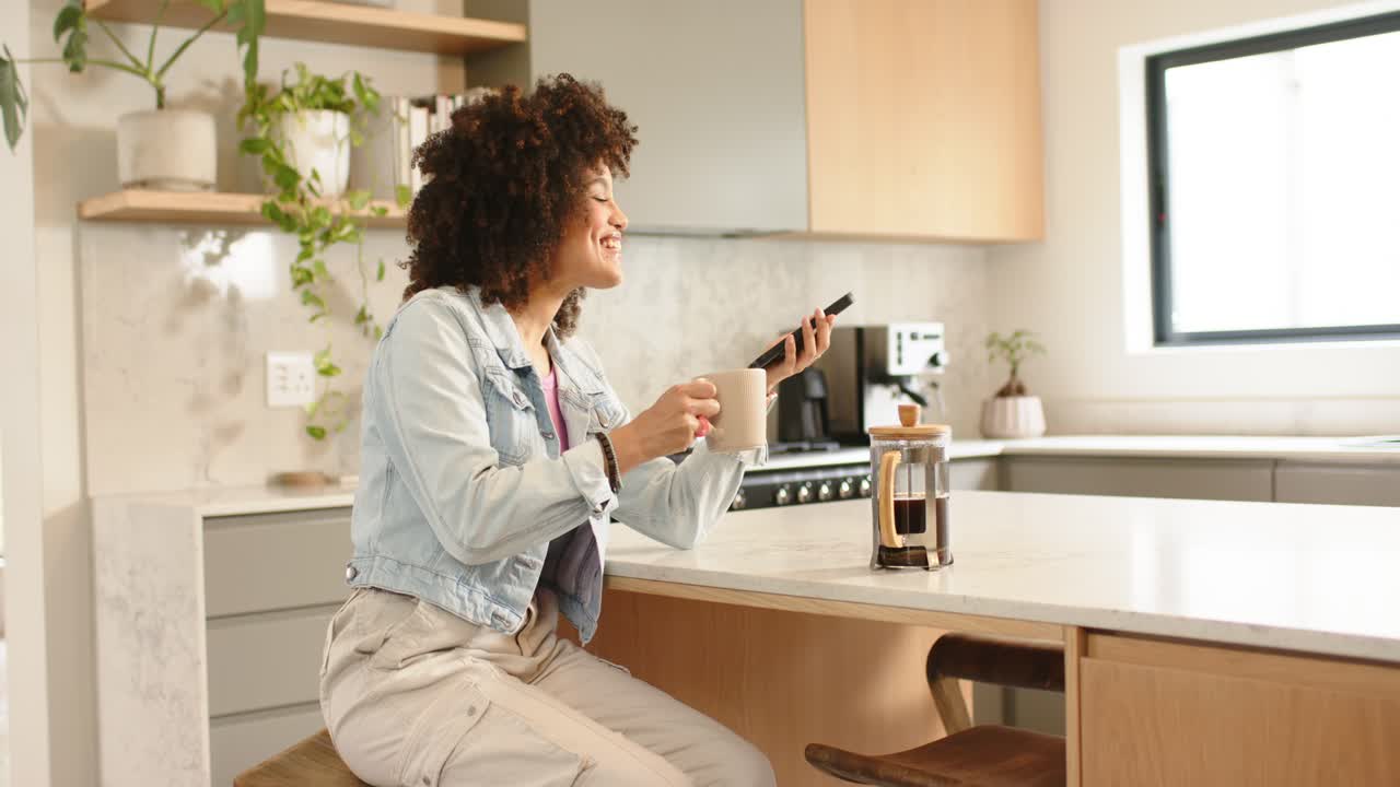 Donna che tiene in mano il telefono e utilizza l'assistente vocale per preparare il caffè con la French press in cucina, sorridente, mentre sorseggia il caffè
