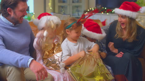 familia con sombreros de santa sentada en el sofá en casa abriendo regalos de navidad