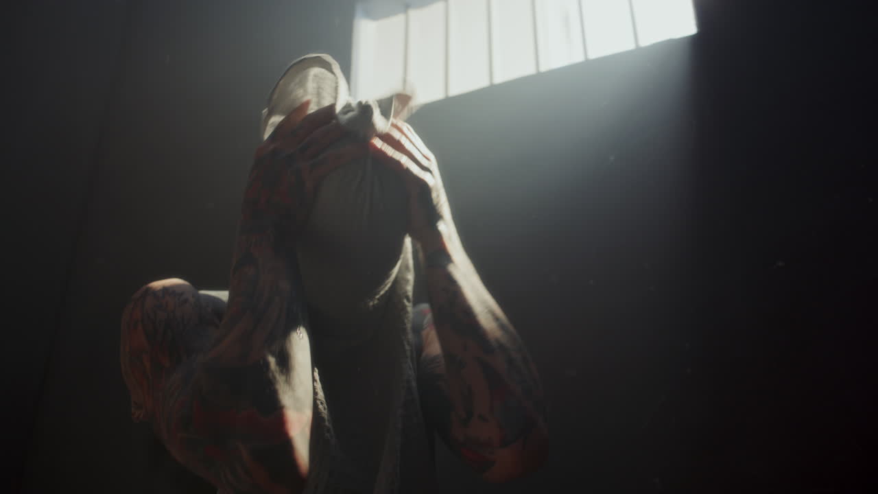 Shirtless Tattooed Inmate Wiping Skin with Towel in Prison Cell