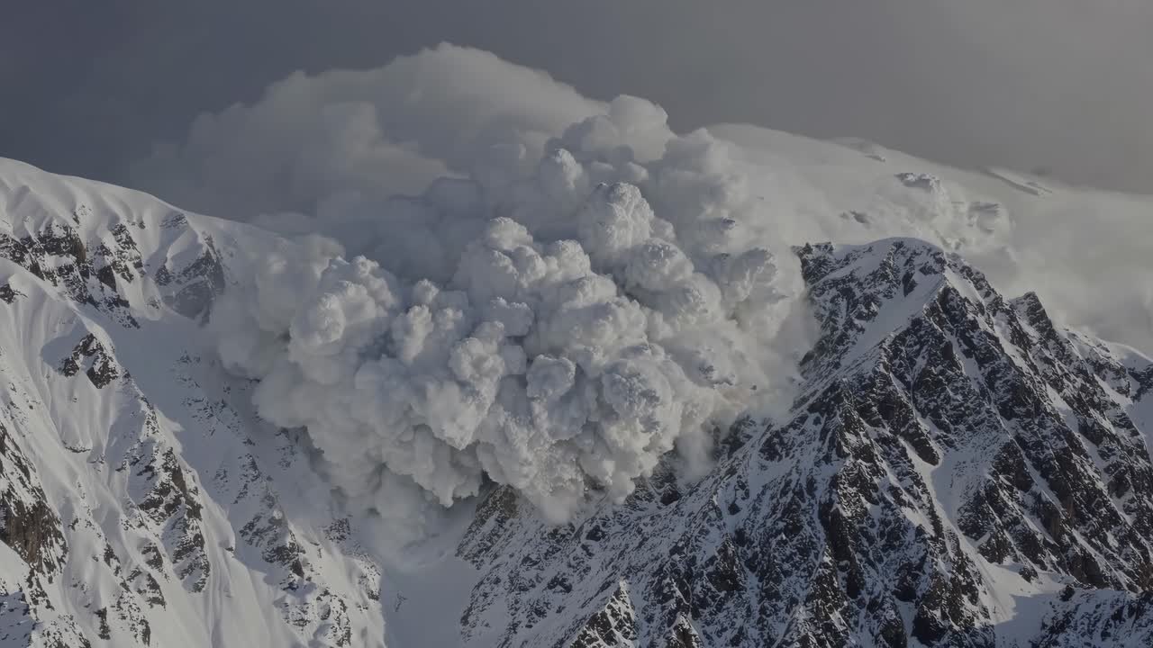 A dramatic aerial video captures a powerful avalanche cascading down rugged, snow-covered mountains