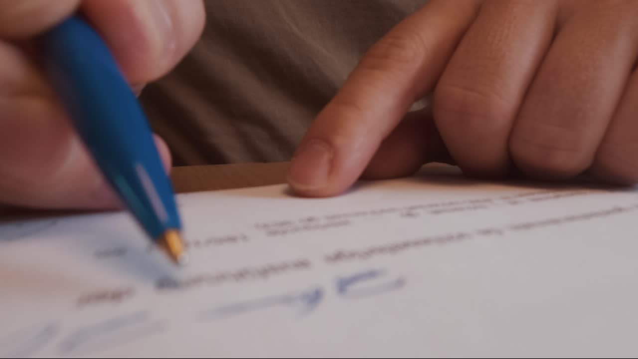 Macro shot of a person signing an official document with a blue pen. Perfect for topics like business agreement, contract signing, approval process, or legal documentation concepts
