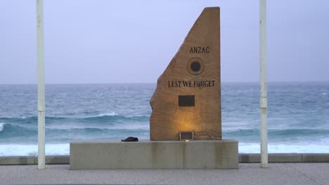 close up to anz war memorial cenotaph carved with lest we forget with rapid and vigorous wave crashing on to the shore in the background at surfers paradise, gold coast, queensland, australia