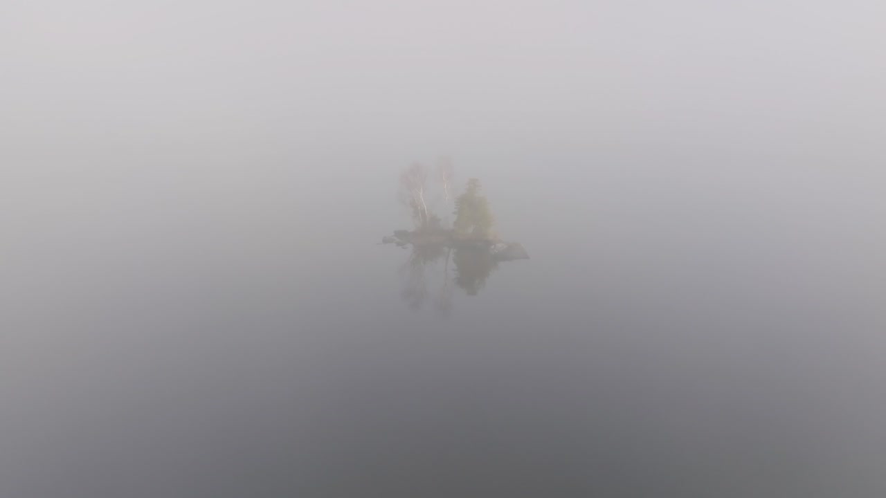 Tiny island with sparse trees dissipates into the fog