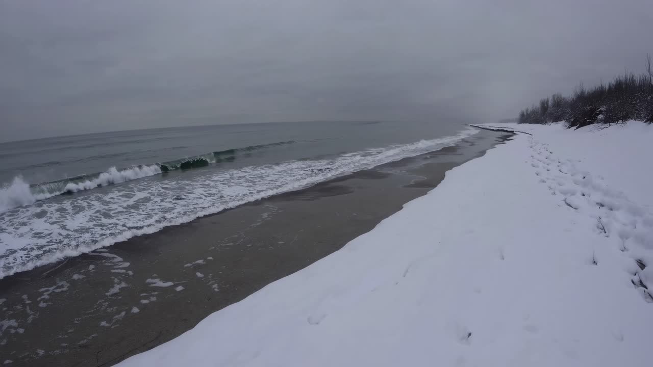 A serene winter beach scene captured from a low-angle, showcasing snow-covered sand and gentle
