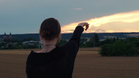 a girl dressed in black pointed at the sky at sunset