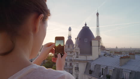 mujer feliz usando un teléfono inteligente tomando fotos disfrutando de compartir la experiencia de las vacaciones de verano en parís fotografiando una hermosa puesta de sol vista de la torre eiffel en el balcón de cerca