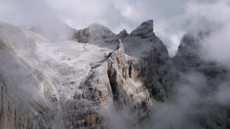 cinematic drone flight through clouds revealing rocky mountain formation in italy - brenta dolomites