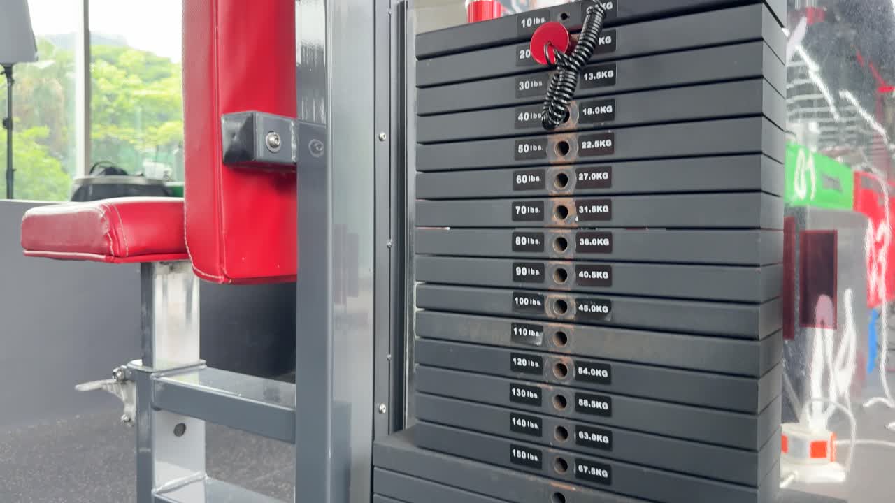 A weight stack in a gym moves up and down, indicating exercise activity. Bright lighting and modern equipment create an energetic atmosphere