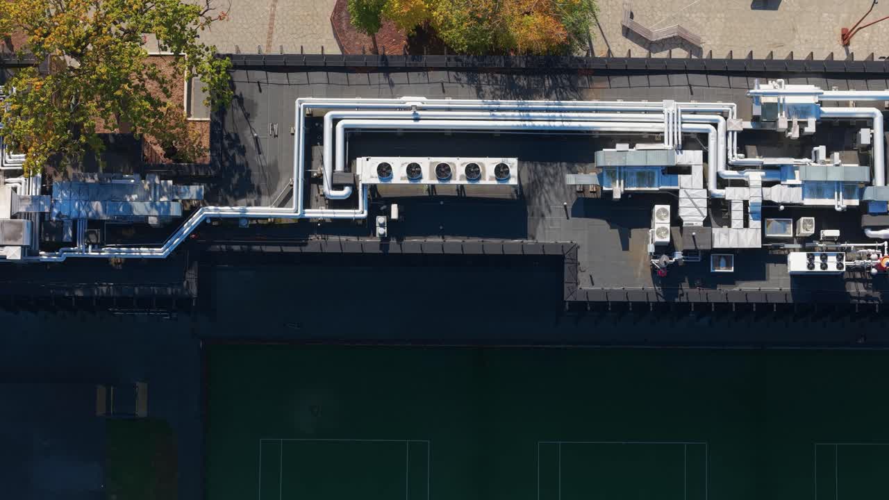 Top-down aerial view of a modern building rooftop featuring HVAC systems, cooling units, and insulated ductwork surrounded by autumn trees in Kaunas, Lithuania