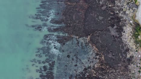 Toma-Aérea-De-Arriba-Hacia-Abajo-De-Los-Acantilados-Blancos-De-La-Playa-De-Dover,-Agua-Azul