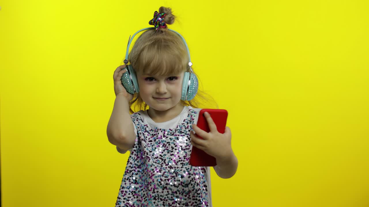 niño baila con teléfono inteligente, escuchando música en auriculares. niña pequeña bailando, teniendo hun