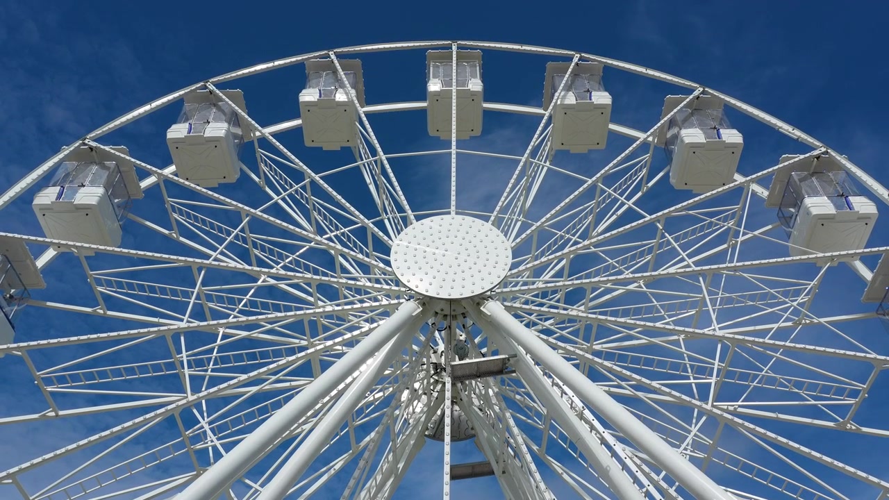 Vue en contre-plongée d'une grande roue blanche moderne tournant lentement sur un ciel bleu éclatant. Attraction estivale cinématographique au port de Weymouth pour du contenu de voyage et de loisirs.