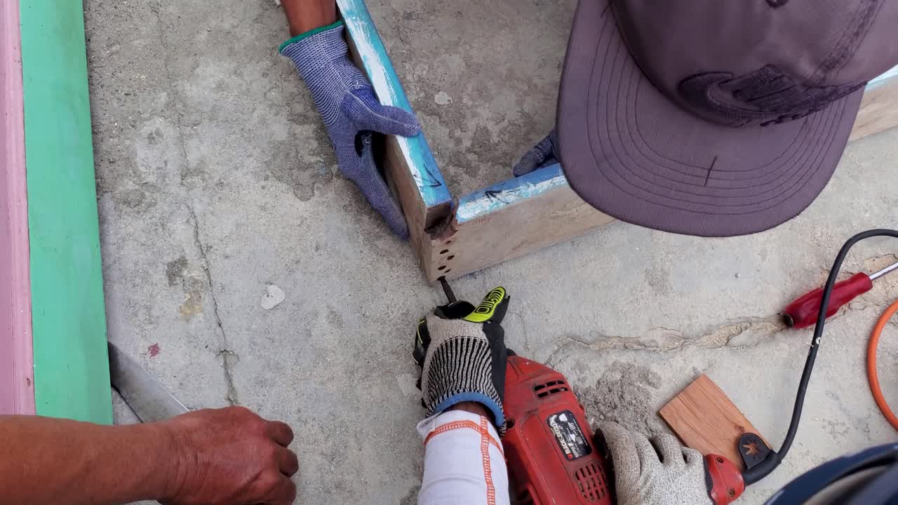 Close up men working with gloves, drill, nails to make wooden door frame, overhead shot