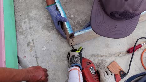 Close-up-men-working-with-gloves,-drill,-nails-to-make-wooden-door-frame,-overhead-shot