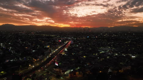 Toma-Aérea-De-Seguimiento-De-Una-Puesta-De-Sol-Nublada-Sobre-La-Avenida-Circuito-Interior-En-La-Ciudad-De-México