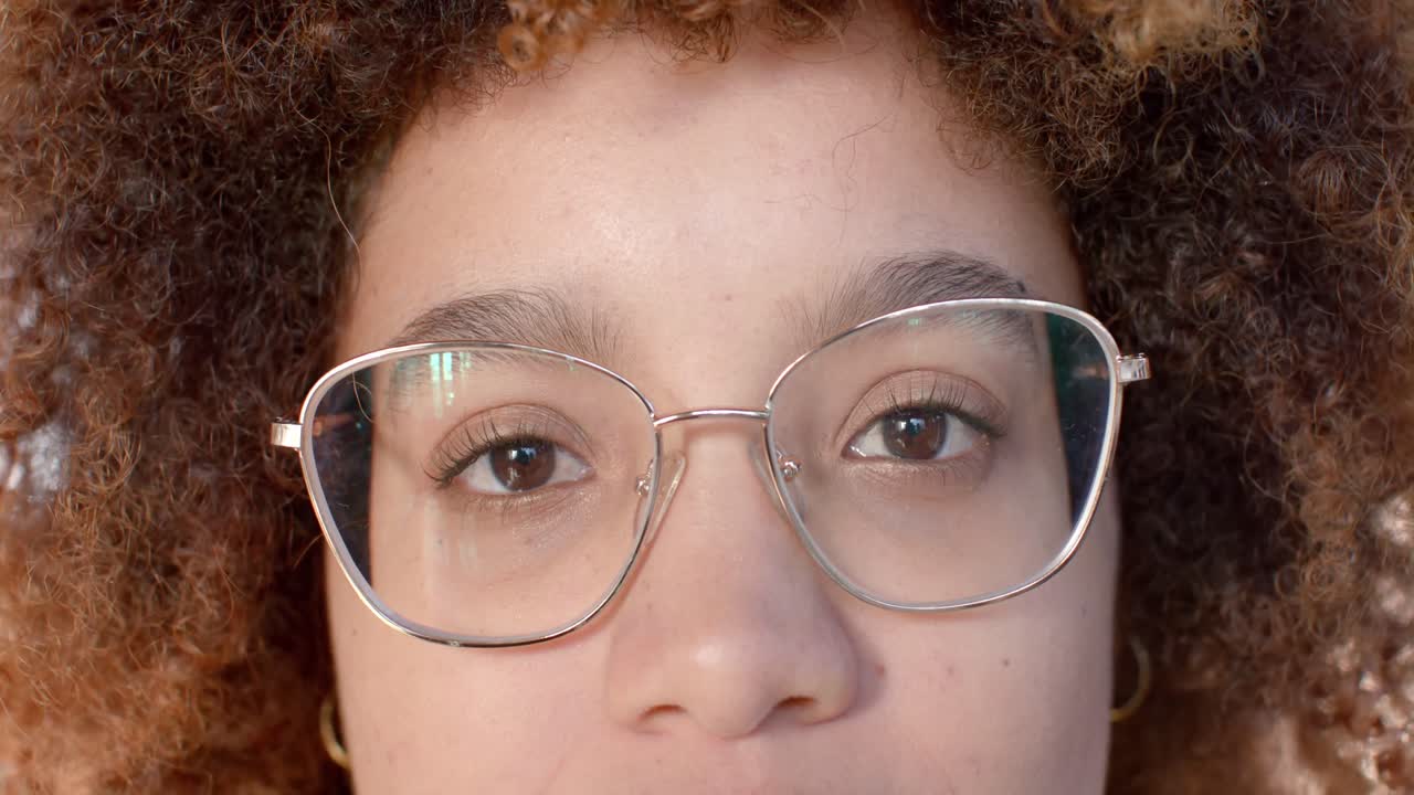 retrato en primer plano de una mujer de negocios casual biracial con gafas abriendo los ojos y sonriendo, en cámara lenta