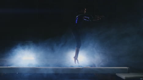 professional gymnast girl performs a jump with a spin on the balance beam in slow motion. smoke blue color in the gym. gymnastics competitions.