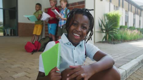 Video-of-happy-african-american-boy-holding-books-in-front-of-school