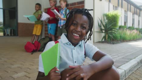 video of happy african american boy holding books in front of school