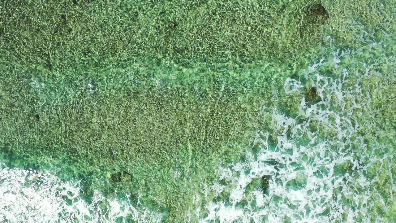 Abstract texture with sea bottom full of pebbles over white sand seen through clear water of turquoise shallow lagoon and white waves, copy space