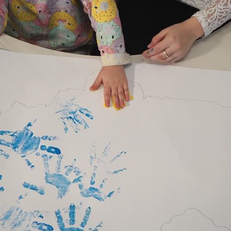 child making hand print on paper. ?olorful designs with hands. little painter.
