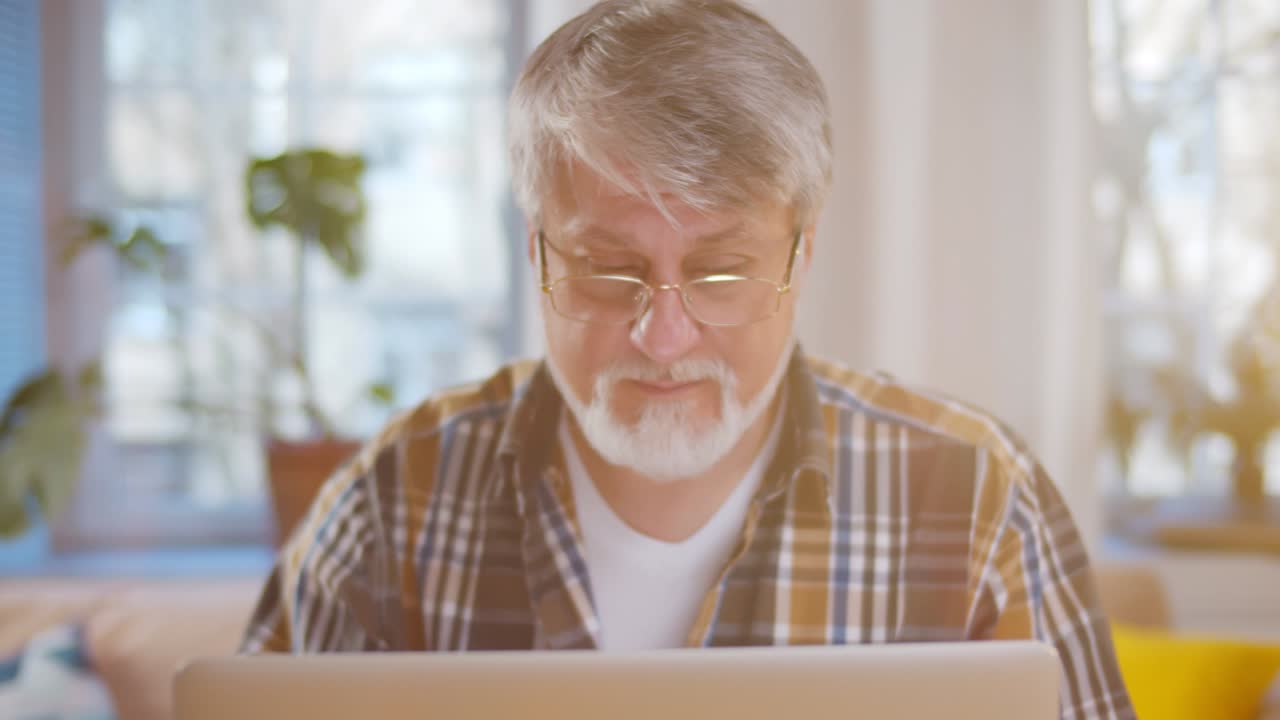 Senior man wearing glasses using computer in living room