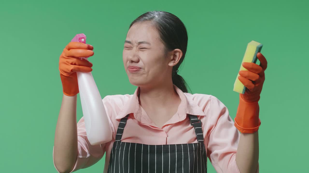 그린 스크린 스튜디오에서 머리가 아프는 스프레이와 부 스폰지를 바라보는 아시안 여성 집주인의 클로즈업