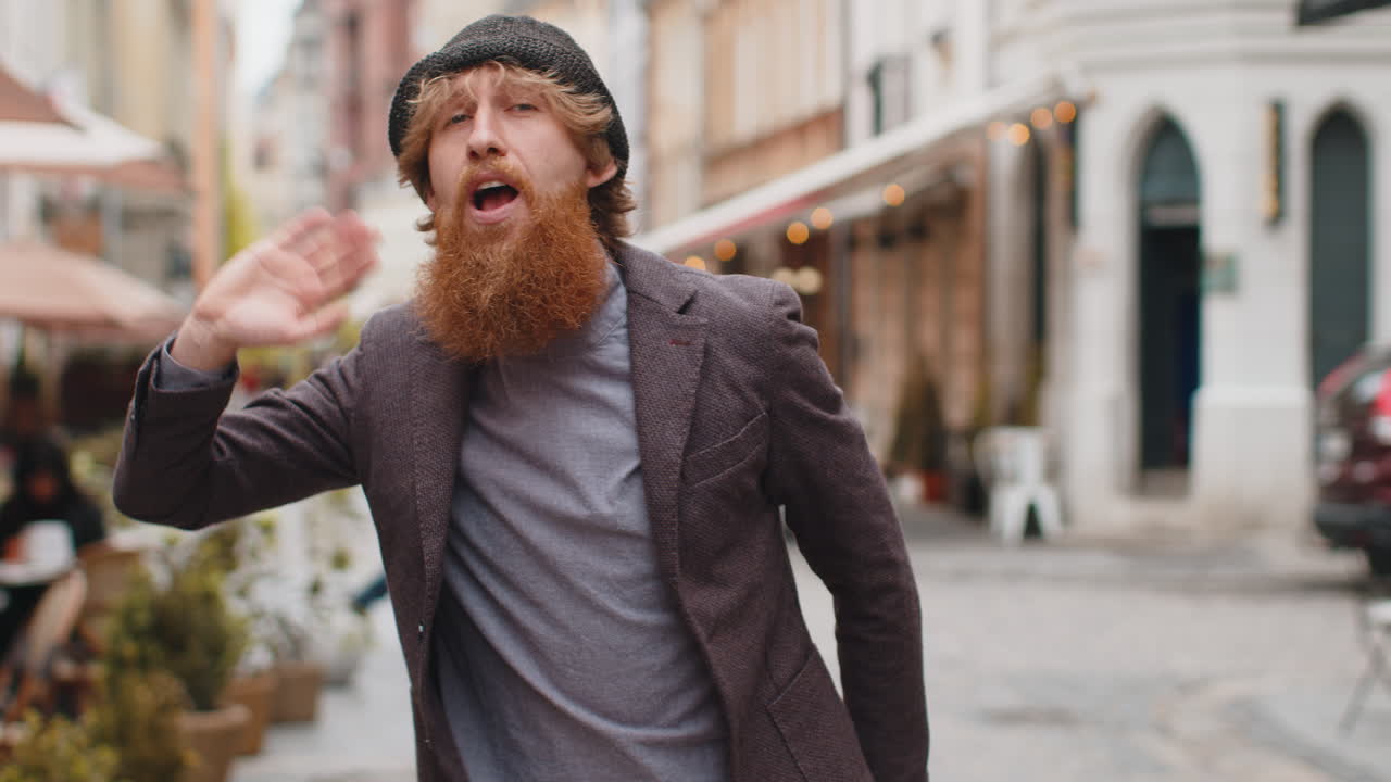 молодой человек улыбается дружелюбно в камеру махает руками привет приветствие или до свидания на городской улице