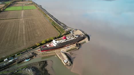 Moored-TSS-Duke-of-Lancaster-in-rural-landscape,-aerial-fly-away-shot