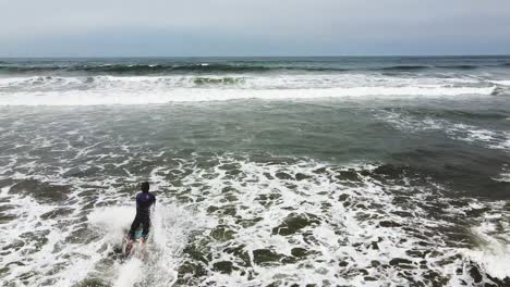 travelling d'un surfeur courant dans la mer tenant sa planche de surf sur une plage de sable