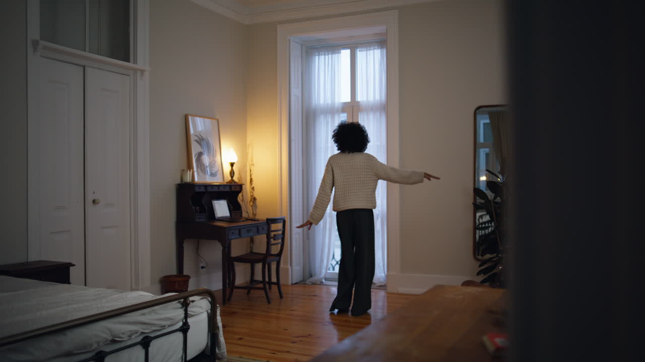 곱슬한 댄서가 몸을 집으로 옮기고 헤드폰을 들고 휴식을 취하는 여성이 주말 저녁을 즐기고 있습니다.