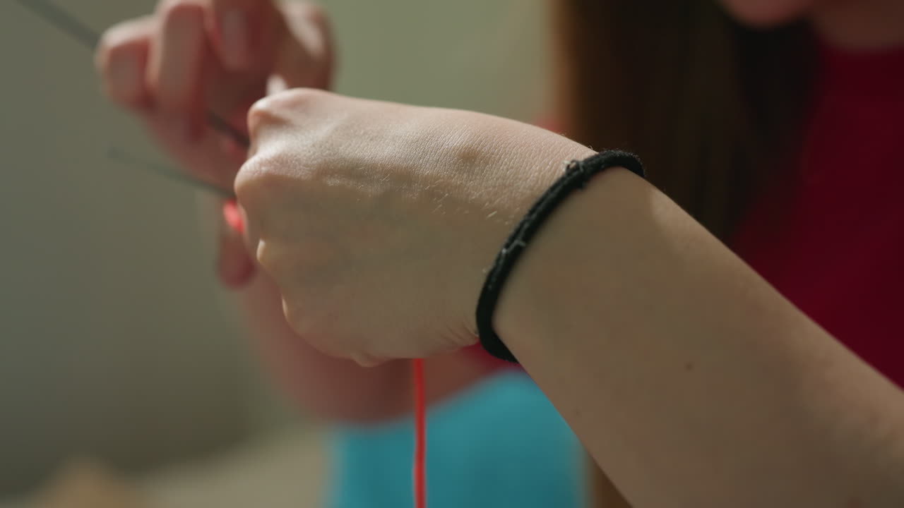 하얀 손이 섬세하게 실을 엮고, 집중한 손은 가는 바늘로 정교한 스티치를 만들어요. 평온한 생활 공간은 세심한 뜨개질 기술에 몰두한 손의 디테일한 움직임을 보여줍니다.