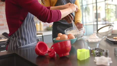 Midsection-of-diverse-couple-in-aprons-baking-in-sunny-kitchen,-slow-motion