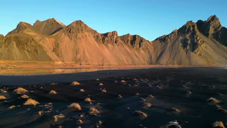 turista disfrutando de la magnífica vista de la cordillera de stokksnes desde la playa negra en islandia en un día soleado, revelando el ascenso aéreo