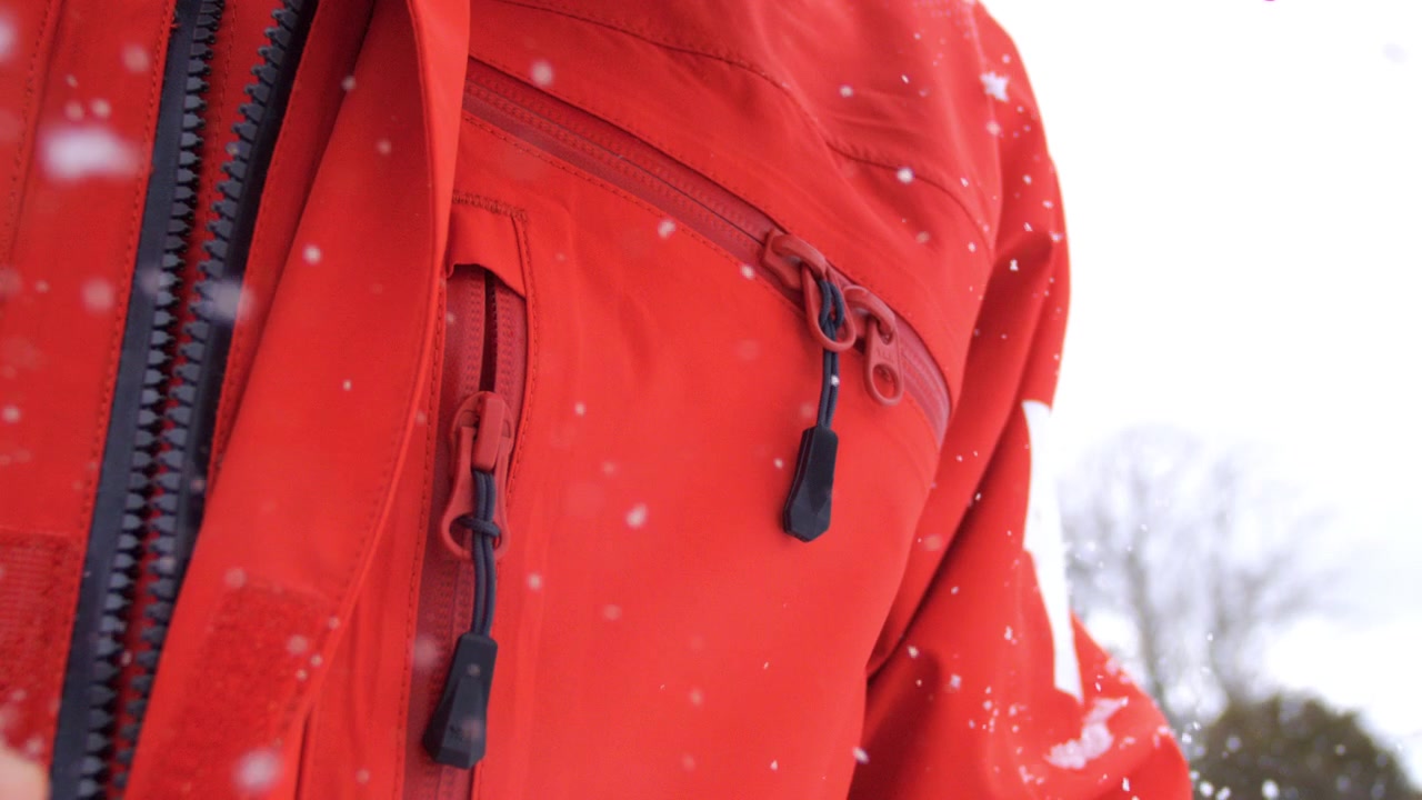 Falling snow surrounds heavy-duty zippered areas of a red winter jacket in close detail