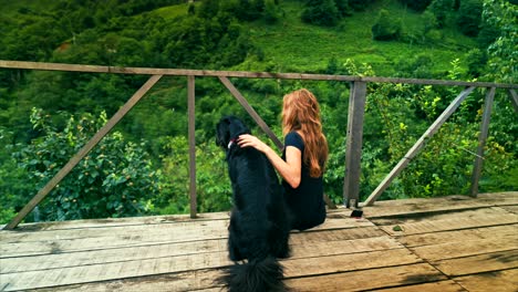 a woman and her dog enjoying a peaceful moment on a wooden deck overlooking a lush, green valley