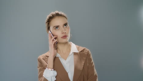 Mujer-Molesta-Hablando-Por-Teléfono-Móvil-Sobre-Fondo-Gris-En-El-Estudio
