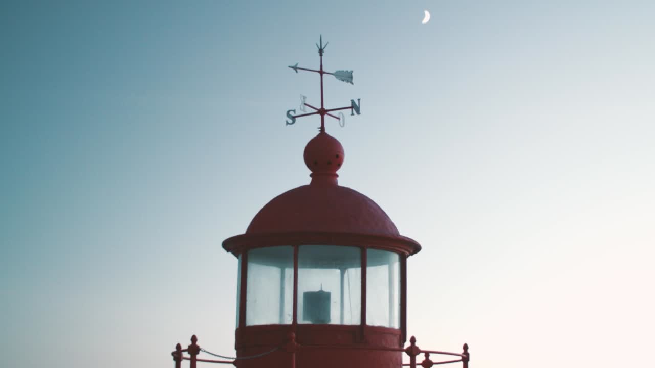 antiguo faro rojo y encantador "farol" con flechas para puntos cardinales y luna en el fondo en el cielo oscuro, nazare en portugal tarde de verano