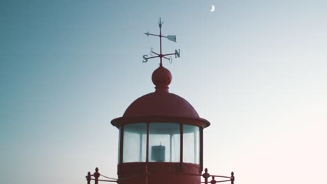 antiguo faro rojo y encantador "farol" con flechas para puntos cardinales y luna en el fondo en el cielo oscuro, nazare en portugal tarde de verano