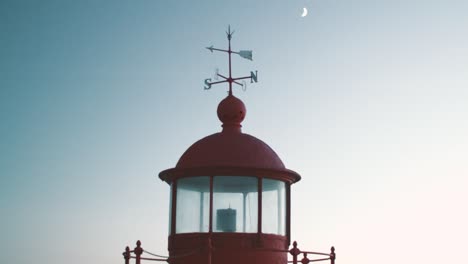 old red and charming "farol" lighthouse with arrows for cardinal points and moon in the background in the dark sky, nazare in portugal late summer evening