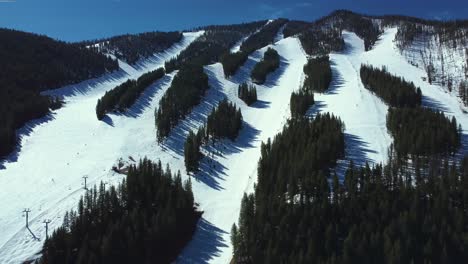 Aerial-View-Of-Mountain-Slopes-Covered-With-Snow-With-Evergreen-Forest-In-Winter