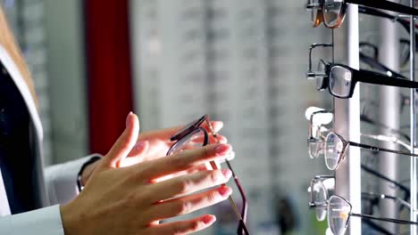 female customer at optical store. woman's hands taking a new pair of stylish eyeglasses from the stand. close-up. vision concept.