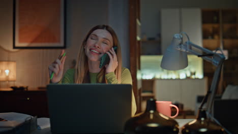 positive remote worker talking mobile phone at desk laptop late evening close up