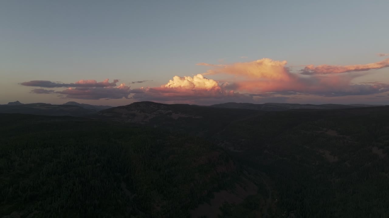 Drone extreme wide shot of the Uinta-Wasatch-Cache National Forest in Utah during a summer sunset, pine trees, Provo River, mountain peaks and clouds rising above the valley