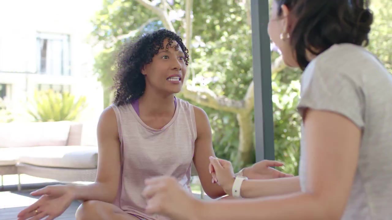 Curly woman sitting facing friend, other woman gesturing, causing particle overlay for health